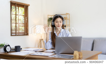 Asian female college student wearing headphones watching live performance or video call teacher teaching on laptop, Conversations with teachers and classmates, Online learning, Study at your own home. Asian female college student wearing headphones watching live performance or video call teacher teaching on laptop, Conversations with teachers and classmates, Online learning, Study at your own home. 98406847