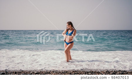 A tourist woman in blue bikini on beach enjoys the turquoise sea during her summer holiday. Rear view. Beach vacation. woman with braids dreadlocks standing with her arms raised enjoying beach ocean. A tourist woman in blue bikini on beach enjoys the turquoise sea during her summer holiday. Rear view. Beach vacation. woman with braids dreadlocks standing with her arms raised enjoying beach ocean. 98407013