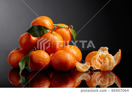 Tangerines or clementines with green leaves on a black background. Tangerines or clementines with green leaves on a black background. 98407064