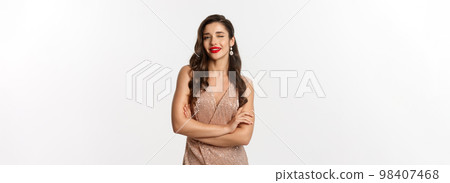 Beautiful woman in evening dress and red lipstick, winking at camera and smiling, celebrating New Year party, standing over white background Beautiful woman in evening dress and red lipstick, winking at camera and smiling, celebrating New Year party, standing over white background 98407468