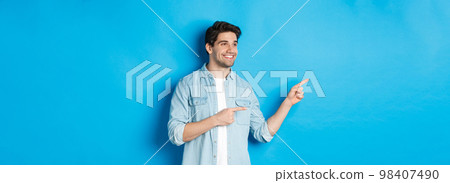 Handsome adult man introduce product, looking and pointing fingers left, promoting something against blue background 98407490