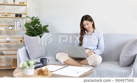 Woman using laptop to work or do homework at home with smiling face in her living room, Creating happiness at work with a smile, Live performance or video call with laptop, Work from home. Woman using laptop to work or do homework at home with smiling face in her living room, Creating happiness at work with a smile, Live performance or video call with laptop, Work from home. 98407560