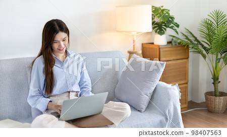 Woman using laptop to work or do homework at home with smiling face in her living room, Creating happiness at work with a smile, Live performance or video call with laptop, Work from home. Woman using laptop to work or do homework at home with smiling face in her living room, Creating happiness at work with a smile, Live performance or video call with laptop, Work from home. 98407563