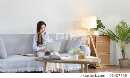 Woman using laptop to work or do homework at home with smiling face in her living room, Creating happiness at work with a smile, Live performance or video call with laptop, Work from home. Woman using laptop to work or do homework at home with smiling face in her living room, Creating happiness at work with a smile, Live performance or video call with laptop, Work from home. 98407566