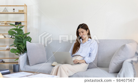 Woman using laptop to work or do homework at home with smiling face in her living room, Creating happiness at work with a smile, Live performance or video call with laptop, Work from home. Woman using laptop to work or do homework at home with smiling face in her living room, Creating happiness at work with a smile, Live performance or video call with laptop, Work from home. 98407567