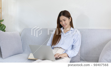 Woman using laptop to work or do homework at home with smiling face in her living room, Creating happiness at work with a smile, Live performance or video call with laptop, Work from home. Woman using laptop to work or do homework at home with smiling face in her living room, Creating happiness at work with a smile, Live performance or video call with laptop, Work from home. 98407568
