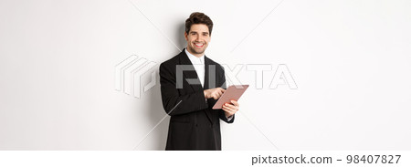 Image of handsome businessman in black suit, using digital tablet and smiling, standing against white background 98407827