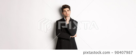 Portrait of handsome and stylish man in suit, thinking and looking at upper left corner, imaging something about christmas holidays, standing over white background 98407987
