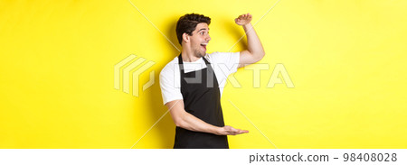 Man looking surprised at something large, standing in black apron against yellow background Man looking surprised at something large, standing in black apron against yellow background 98408028