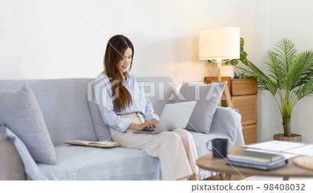 Woman using laptop to work or do homework at home with smiling face in her living room, Creating happiness at work with a smile, Live performance or video call with laptop, Work from home. Woman using laptop to work or do homework at home with smiling face in her living room, Creating happiness at work with a smile, Live performance or video call with laptop, Work from home. 98408032