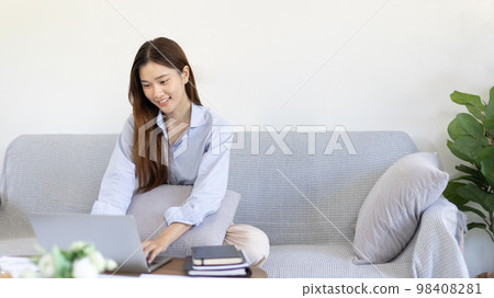 Woman using laptop to work or do homework at home with smiling face in her living room, Creating happiness at work with a smile, Live performance or video call with laptop, Work from home. Woman using laptop to work or do homework at home with smiling face in her living room, Creating happiness at work with a smile, Live performance or video call with laptop, Work from home. 98408281