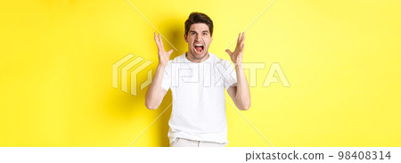 Angry man yelling and shaking hands, grimacing with hatred, standing hateful against yellow background Angry man yelling and shaking hands, grimacing with hatred, standing hateful against yellow background 98408314