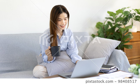 Beautiful Asian woman working on laptop and sipping coffee with smiling face in her home, Creating happiness at work with a smile, Freelancer working at home happily, Work from home. Beautiful Asian woman working on laptop and sipping coffee with smiling face in her home, Creating happiness at work with a smile, Freelancer working at home happily, Work from home. 98408517