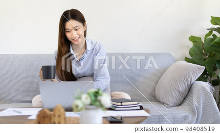 Beautiful Asian woman working on laptop and sipping coffee with smiling face in her home, Creating happiness at work with a smile, Freelancer working at home happily, Work from home. 98408519