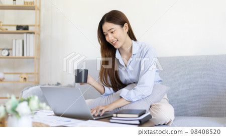 Beautiful Asian woman working on laptop and sipping coffee with smiling face in her home, Creating happiness at work with a smile, Freelancer working at home happily, Work from home. 98408520