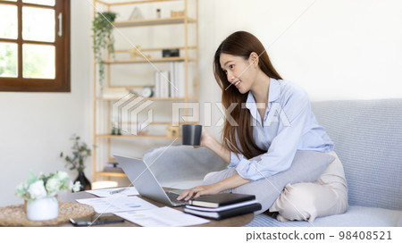 Beautiful Asian woman working on laptop and sipping coffee with smiling face in her home, Creating happiness at work with a smile, Freelancer working at home happily, Work from home. Beautiful Asian woman working on laptop and sipping coffee with smiling face in her home, Creating happiness at work with a smile, Freelancer working at home happily, Work from home. 98408521
