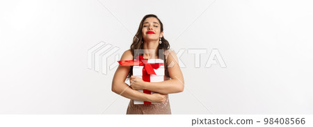 Holidays, celebration concept. Happy and thankful woman hugging Christmas gift, wearing luxury dress, receiving New Year present, standing over white background 98408566