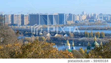 Autumn modern city view of Kyiv on sunny day, static wide footage. Developing city with new buildings, construction cranes, backdrop of modern office buildings panorama. Bridge over blue Ukraine river 98409164