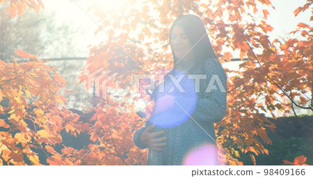 Pregnant woman in sun glare light autumn outdoor. Happy girl with pregnant belly standing in orange fall foliage. Mother expecting child. Maternity, motherhood care in natural park. Tranquil pregnancy 98409166