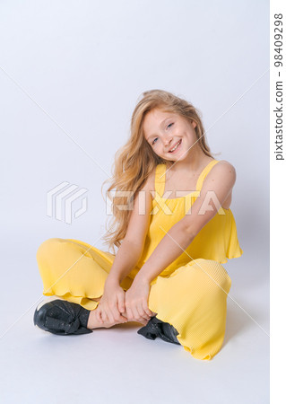 Studio portrait pretty girl with curly hair sitting on floor in studio smiling Studio portrait pretty girl with curly hair sitting on floor in studio smiling 98409298