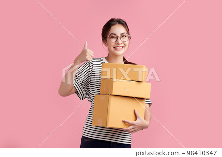 Beautiful Young Asian woman holding parcel box isolated on pink background, Delivery courier and shipping service concept. Beautiful Young Asian woman holding parcel box isolated on pink background, Delivery courier and shipping service concept. 98410347