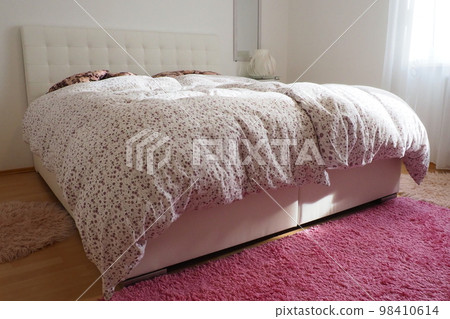 Cozy compact bedroom with white furniture, pink carpet and tulle curtains. Fluffy feather blanket is thrown over the bed. Romantic morning. Double bed with upholstered headboard. Light from the window Cozy compact bedroom with white furniture, pink carpet and tulle curtains. Fluffy feather blanket is thrown over the bed. Romantic morning. Double bed with upholstered headboard. Light from the window 98410614