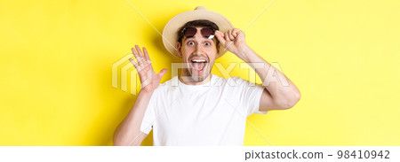 Concept of tourism and holidays. Excited man tourist take-off sunglasses and looking amazed at promo offer, standing over yellow background Concept of tourism and holidays. Excited man tourist take-off sunglasses and looking amazed at promo offer, standing over yellow background 98410942