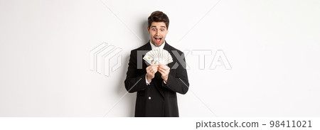 Image of handsome bearded guy in black suit, looking at money with excitement, standing over white background Image of handsome bearded guy in black suit, looking at money with excitement, standing over white background 98411021
