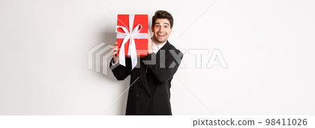 Handsome man in black suit, receiving christmas gift, smiling amazed, standing against white background Handsome man in black suit, receiving christmas gift, smiling amazed, standing against white background 98411026