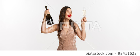 Winter holidays celebration concept. Excited beautiful woman in dress raising glass of champagne for toast, enjoying Christmas party, standig over white background 98411622