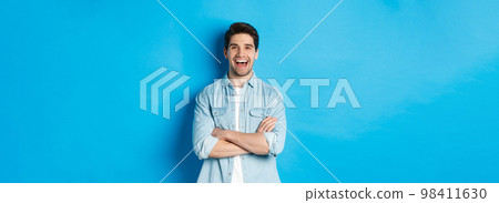 Handsome guy with beard, wearing casual outfit, laughing and looking at something funny, standing against blue background Handsome guy with beard, wearing casual outfit, laughing and looking at something funny, standing against blue background 98411630