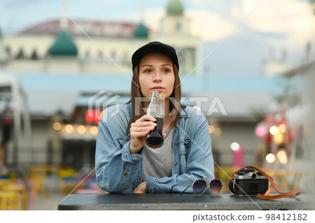 Attractive caucasian woman in hat and jean jacket drinking cola while sitting at street market in Chiang Mai Northern Thailand Attractive caucasian woman in hat and jean jacket drinking cola while sitting at street market in Chiang Mai Northern Thailand 98412182