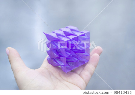 Person holding a abstract model printed on a 3D printer from purple plastic on his hand on gray background close-up. Concept modern printing technology 98413455