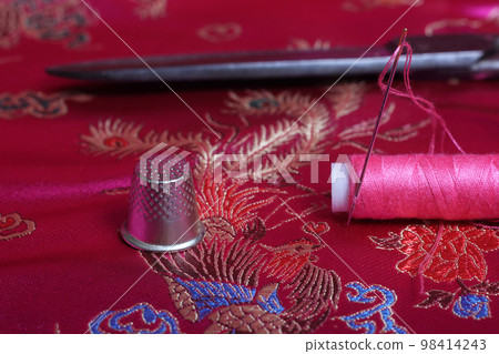 Spool of Pink Thread and Thimble on Vintage Pink Satin Fabric 98414243