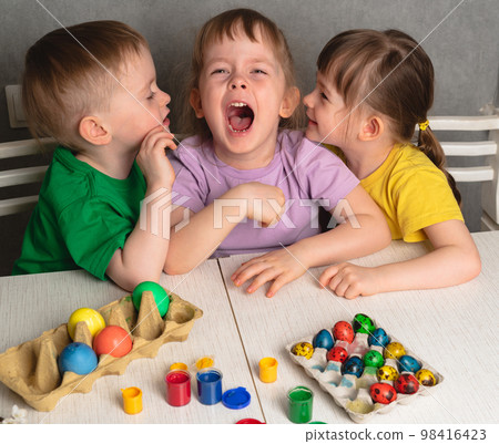 Children talking and laughing at the table with Easter eggs. Brother and sisters prepare for the Easter holiday, paint eggs. 98416423