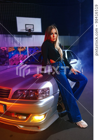 Young beautiful woman with straight long hair posing near white sport car in neon light Young beautiful woman with straight long hair posing near white sport car in neon light 98416519