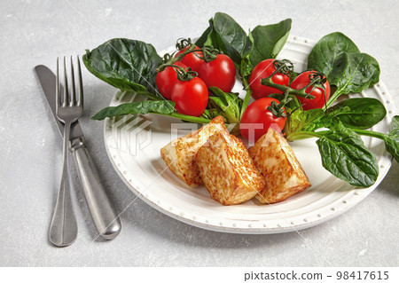 Fried curd cheese mozzarella halloumi with green spinach and cherry tomatoes on a branch with cutlery 98417615