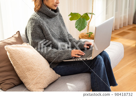 A middle-aged woman sitting on a sofa and working on a computer A middle-aged woman sitting on a sofa and working on a computer 98418732