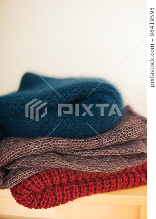 A stack of knitted woolen products lies on a wooden stool 98419593