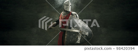 Banner. Serious brutal bearded man, medieval warrior and knight with dirty wounded face holding big sword over dark background. Concept of courage, history Banner. Serious brutal bearded man, medieval warrior and knight with dirty wounded face holding big sword over dark background. Concept of courage, history 98420394