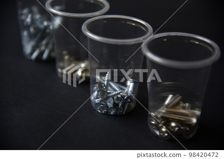 Construction bolts and screws in plastic cups on a black background. Construction accessories. Construction bolts and screws in plastic cups on a black background. Construction accessories. 98420472