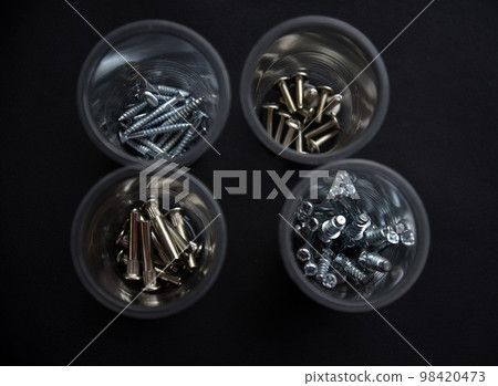 Construction bolts and screws in plastic cups on a black background. Construction accessories. Construction bolts and screws in plastic cups on a black background. Construction accessories. 98420473