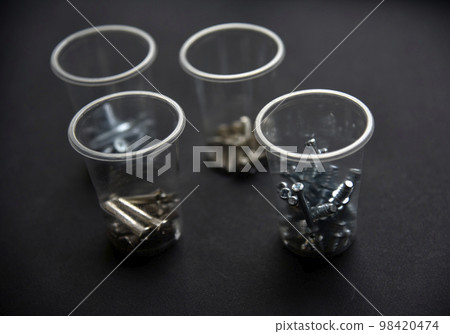 Construction bolts and screws in plastic cups on a black background. Construction accessories. 98420474