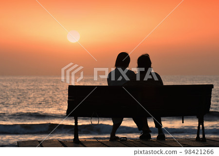 Back view of a couple silhouette, watching sunset on the beach Back view of a couple silhouette, watching sunset on the beach 98421266