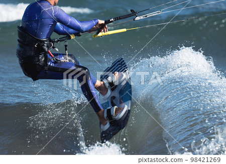 Athletic man jumping on kite surf board on a sea waves. Kiteboarding man among waves quickly goes. Watersport adrenaline fun adventure acitivity 98421269