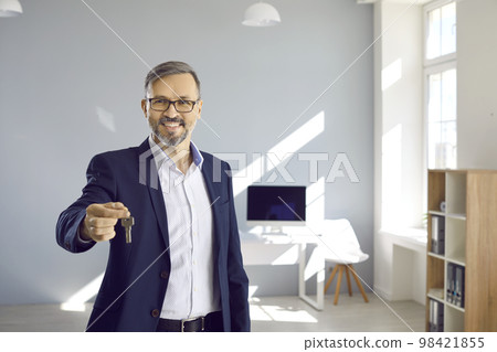 Portrait of friendly male realtor who shows keys to house or office that he has sold or leased. 98421855
