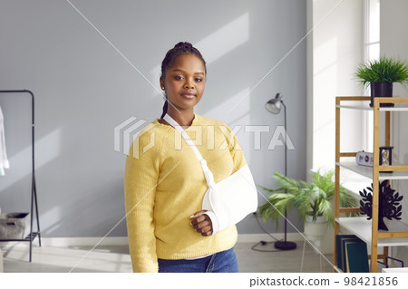 Portrait of young African American woman who wears bandage on her broken arm at home. 98421856