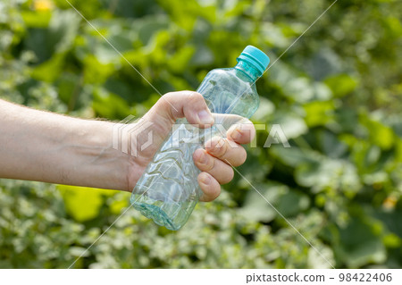 Hand holding crumpled empty plastic bottle in the park 98422406