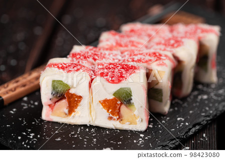 Asian sweet dessert maki sushi close-up - Roll with fruits and cream cheese with coconut flakes and topping 98423080