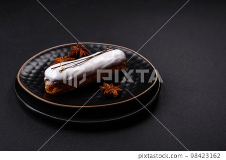 Delicious fresh profiterole or eclair with chocolate on a black ceramic plate 98423162